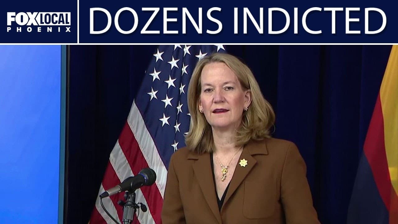 A state official speaks at a podium with U.S. and Arizona flags during a press conference announcing dozens of indictments in the historic health care fraud takedown.