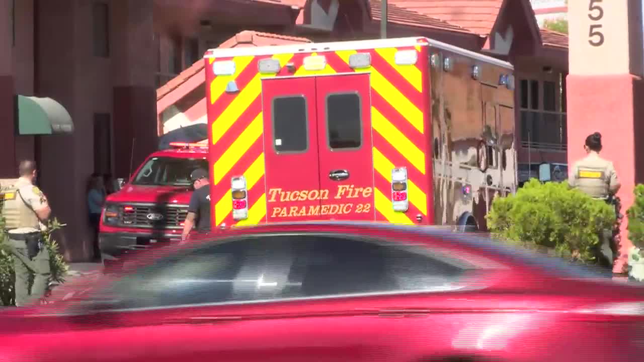 A Tucson Fire ambulance and first responders at the scene following a motorcycle crash near Kolb and 29th; a passing car is visible in the foreground.