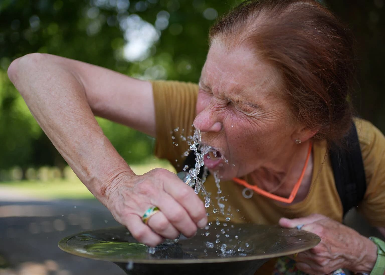A woman drinks from a public water fountain to cool off, illustrating precautions residents are taking during the upcoming heat alerts.