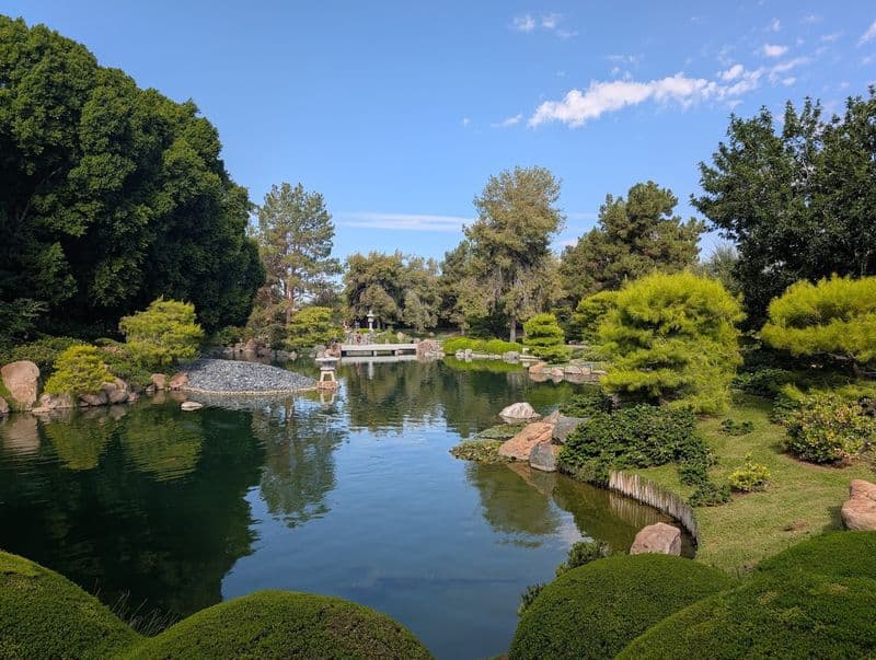 Tranquil pond with manicured shrubs, stone lantern and footbridge at the 3.5-acre Arizona garden, illustrating the garden’s tranquil, storybook setting.