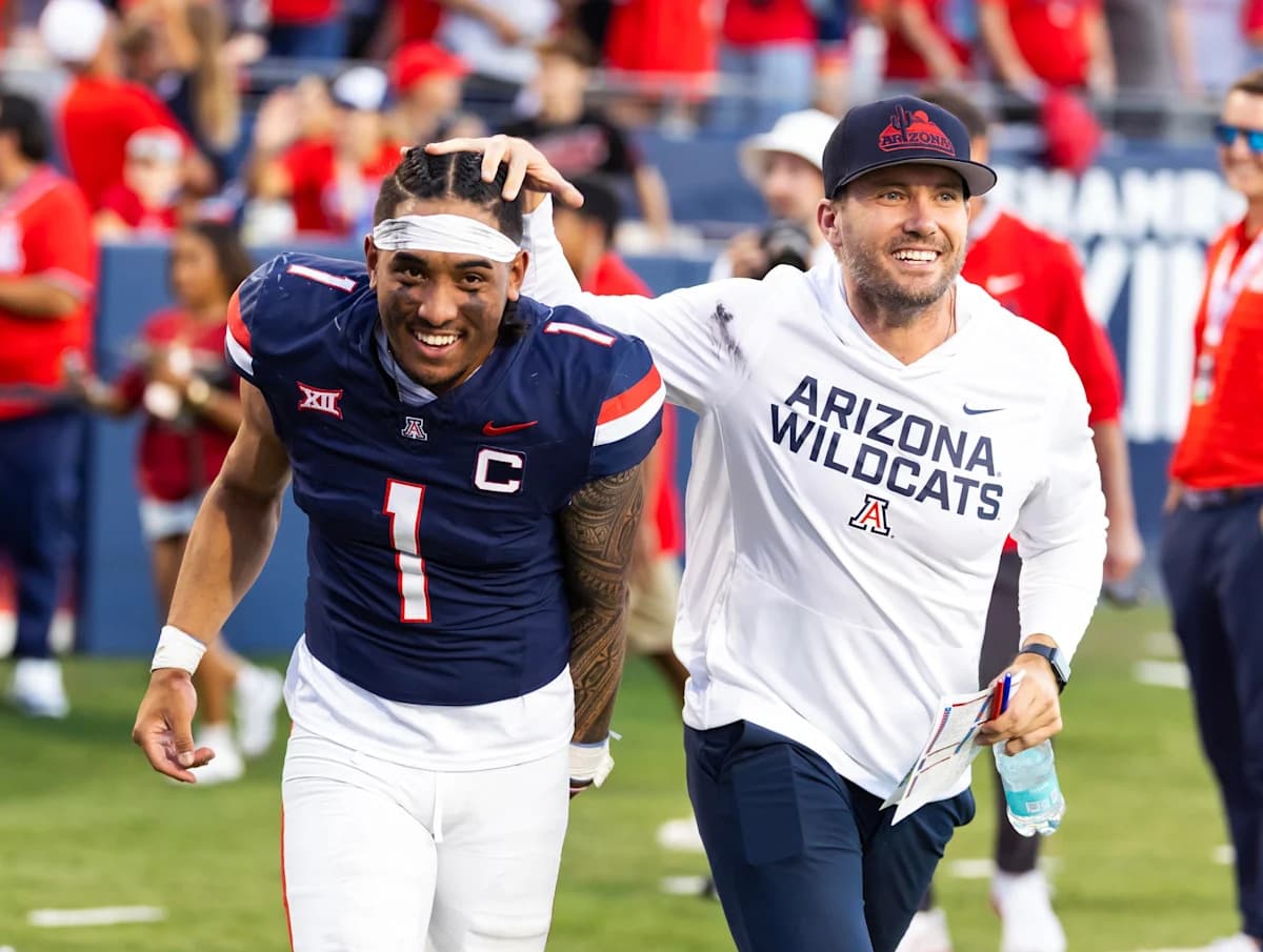An Arizona coach (unidentified) celebrates on the field with a player after a game — a moment that underscores the coaching continuity the program retained heading into the 2026 season.