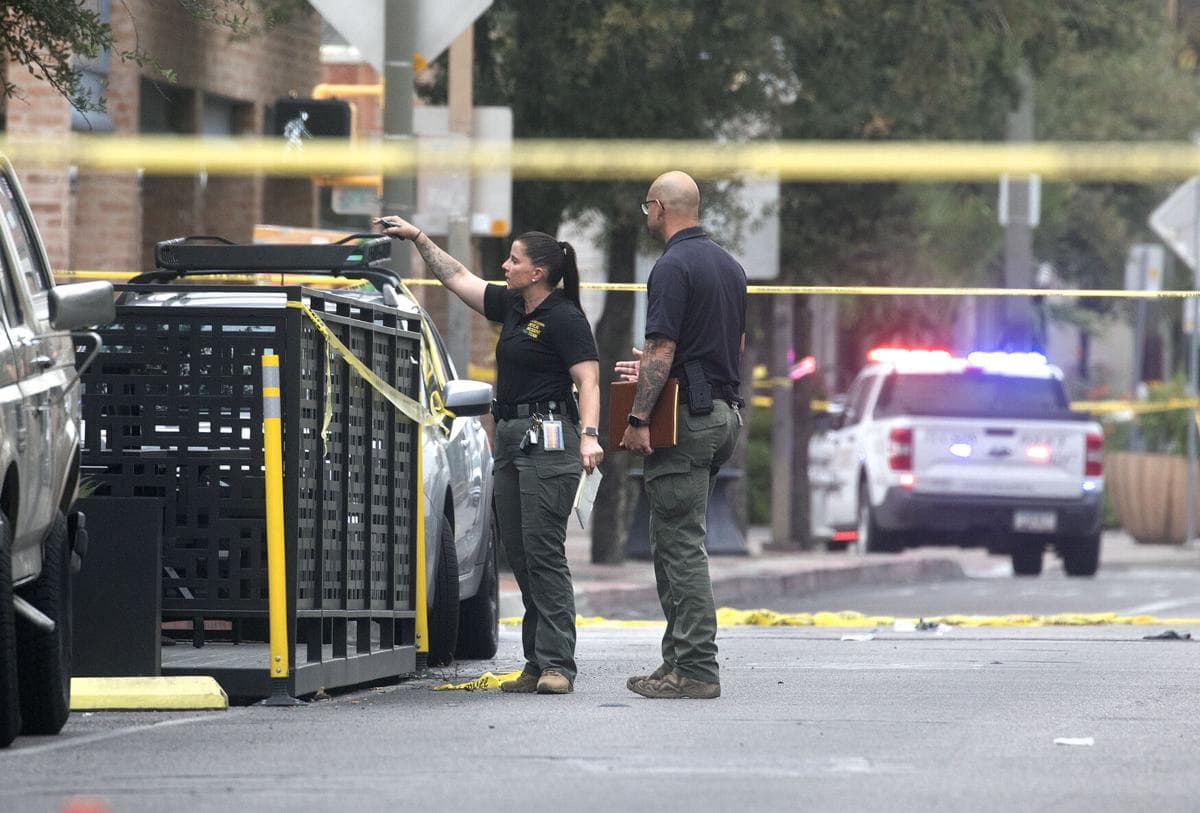 Investigators confer near a cordoned-off street with police vehicles and flashing lights in downtown Tucson following the shooting and the subsequent officer-involved shooting of a suspect.