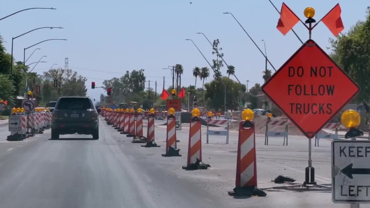 Construction barrels and signage along Val Vista Drive in Mesa as ongoing roadwork narrows lanes and disrupts local businesses.