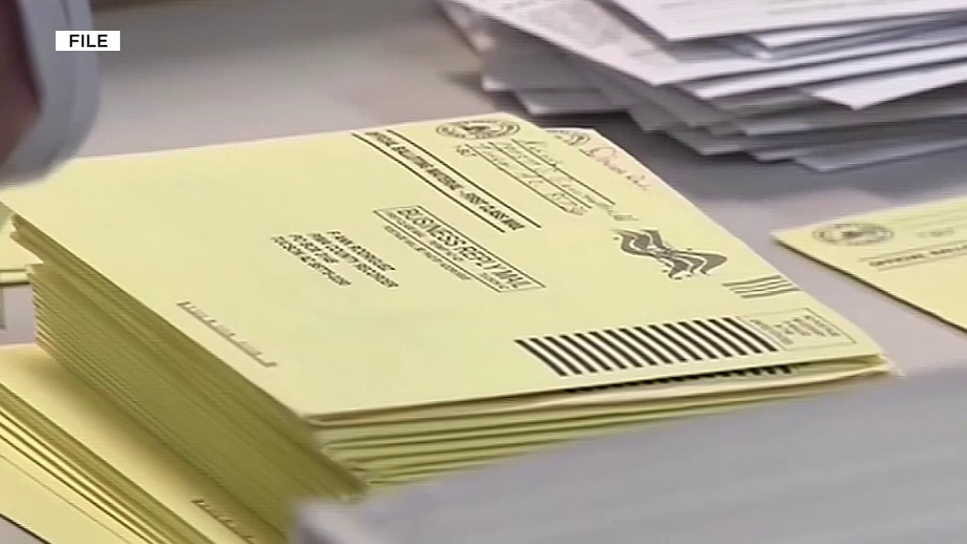 Stack of mail‑in ballot return envelopes at an elections processing table; Arizona officials are urging voters to mail ballots by Tuesday, July 14 so they meet the July 21 primary deadline.