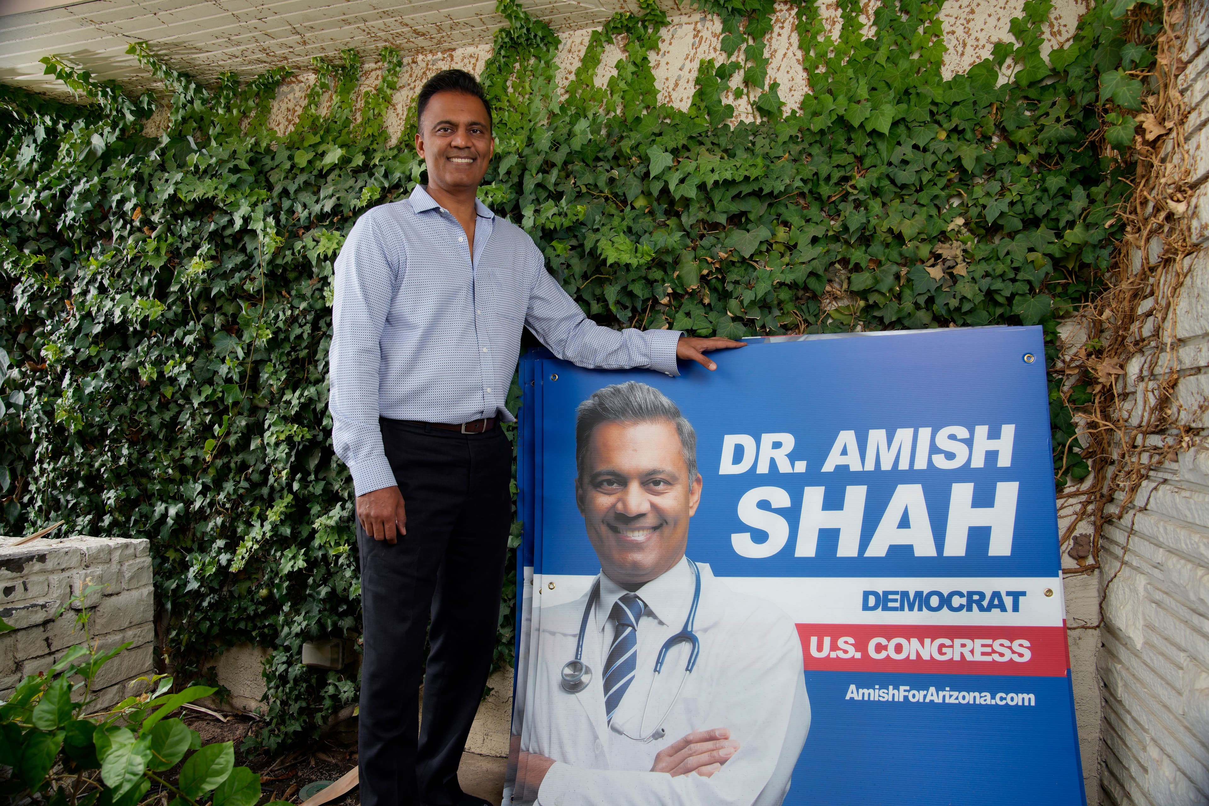 Democratic candidate for Arizona’s U.S. House stands beside a large campaign sign outside a residence after primary-night returns.
