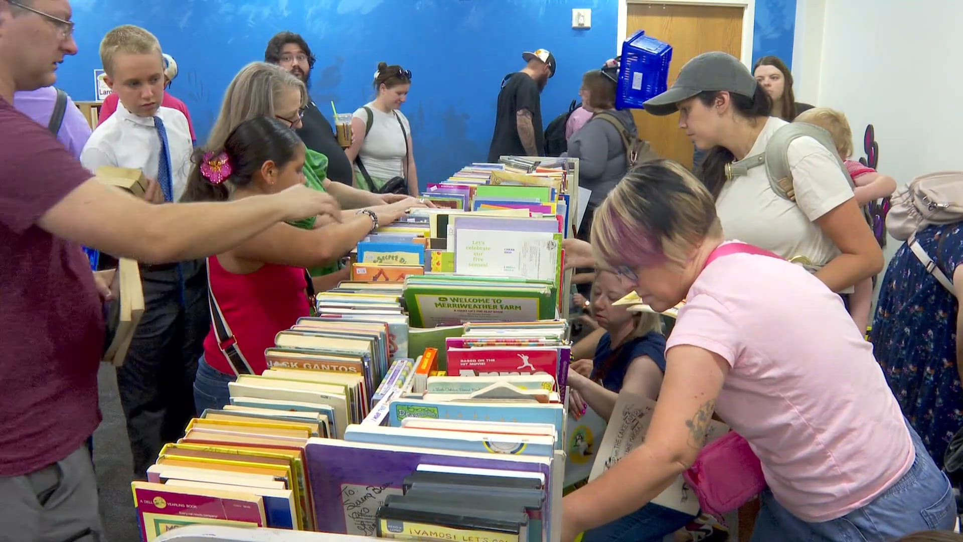 Shoppers browse tables of children's and young‑adult books at a local sale, illustrating reader interest ahead of new releases like Katharine McGee’s 'Ungodly Rich.'