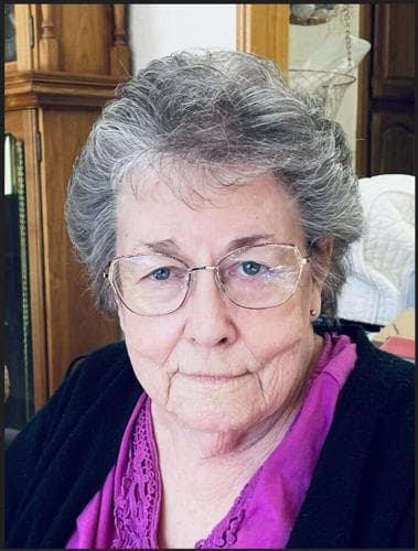 Portrait published with the obituary: close-up of an elderly woman wearing glasses and a purple blouse, seated indoors.