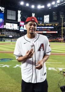 Peat on the field holding the game ball and smiling after throwing the ceremonial first pitch.