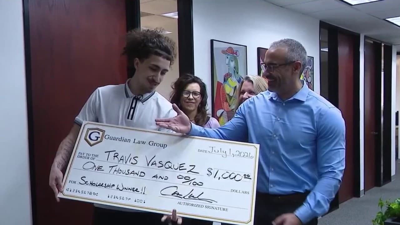 A Phoenix student accepts an oversized $1,000 scholarship check from Guardian Law Group during a presentation at the firm's office.