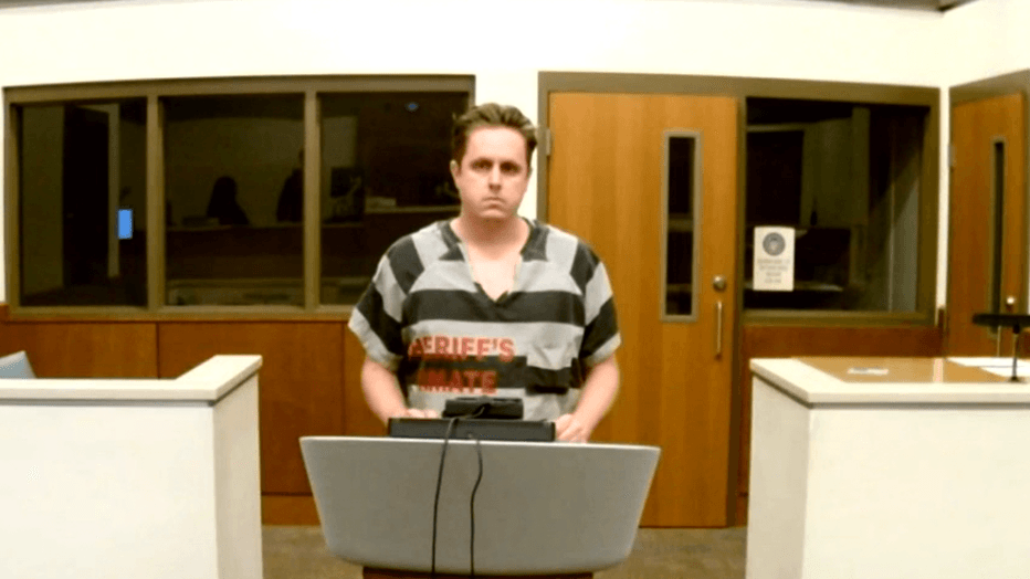 The man accused appears at a Maricopa County courtroom podium in jail attire during an arraignment; police say he was arrested after a woman was allegedly stabbed at a Mesa apartment.