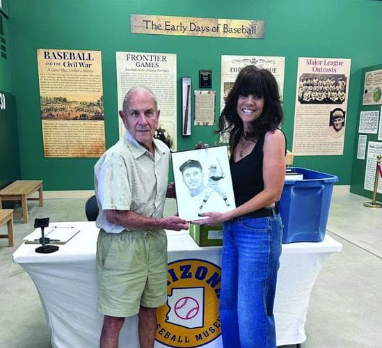 A Mesa artist (right) presents one of her baseball portraits to an Arizona Baseball Museum representative during a preview of the upcoming exhibit.