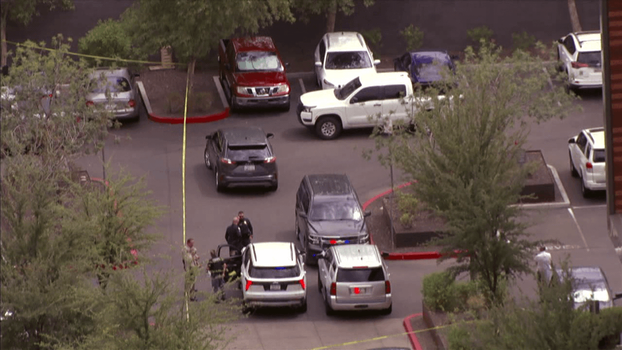 Law enforcement officers and multiple vehicles gathered in a central Phoenix parking lot, with yellow crime-scene tape visible, after a DPS detective-involved shooting.