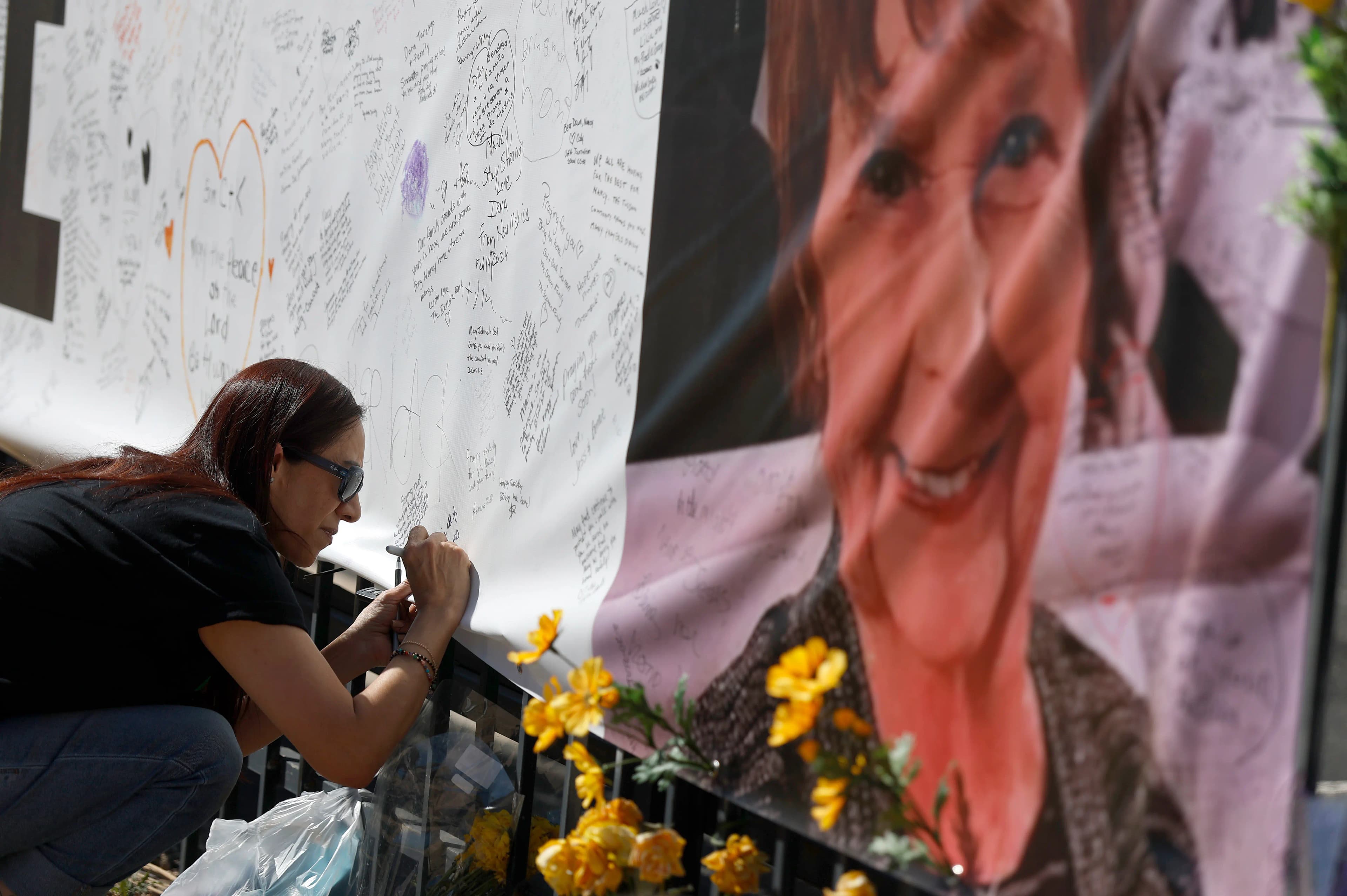 A member of the public signs a memorial banner with a large photo of Nancy Guthrie outside KVOA in Tucson, Ariz., March 3, 2026, as the community responds during the ongoing investigation into her disappearance.