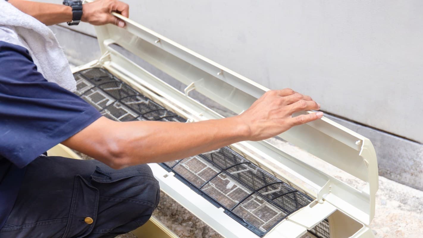 A technician opens and inspects the front panel and filter of an air‑conditioning unit — the type of repair and replacement work AllThrive 365 provided after an Arizona woman endured nearly three years with indoor temperatures in the high 90s.