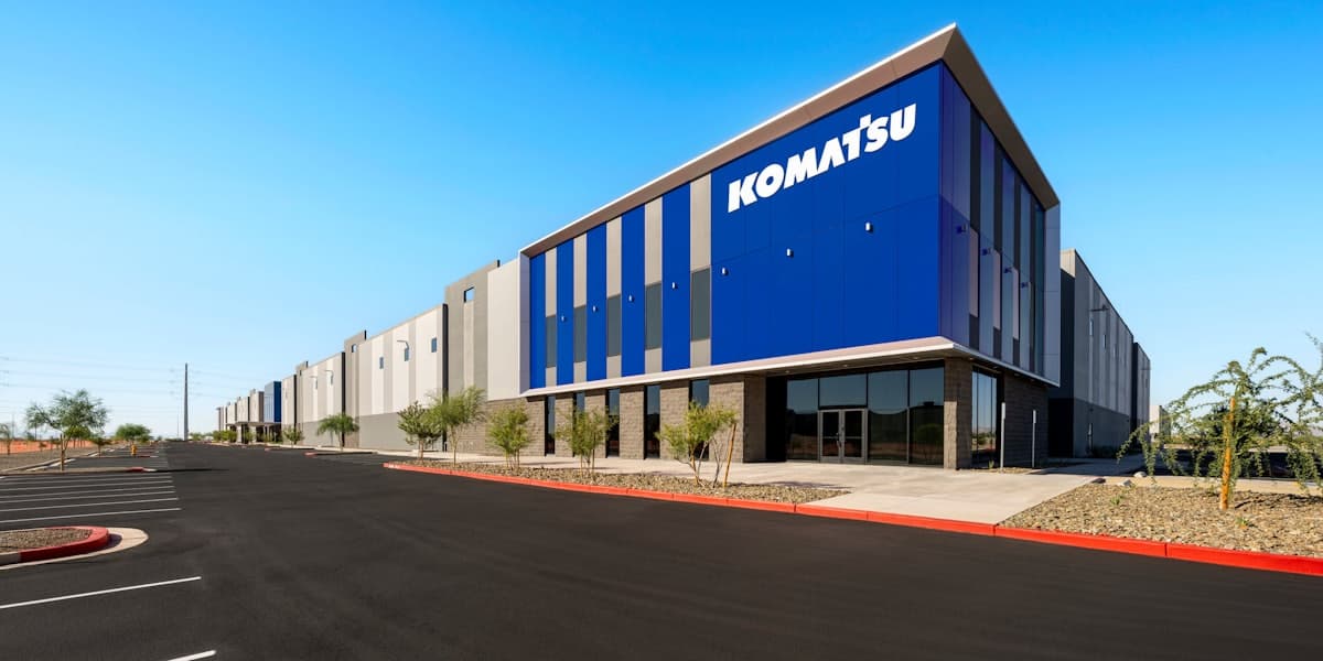 Komatsu-branded exterior of the new parts distribution facility, showing the blue company signage on the warehouse facade and adjacent parking area in Arizona.