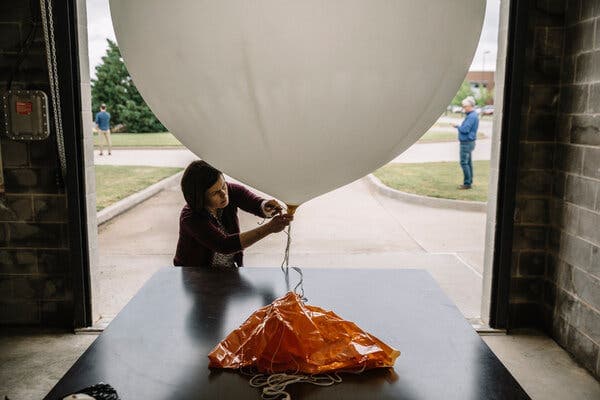 A technician prepares a weather balloon and its parachute inside a garage, equipment used to collect upper‑air moisture data for forecasts.