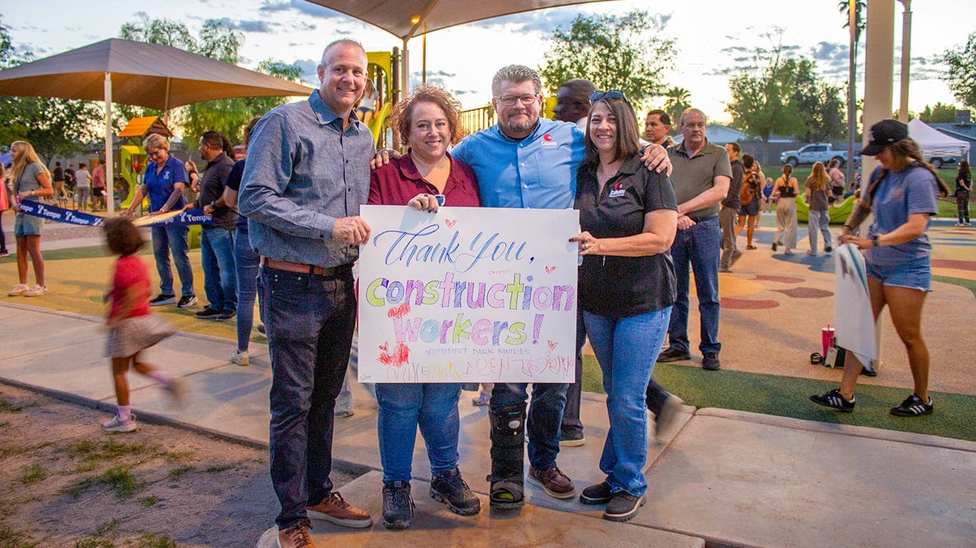 Residents and officials hold a “Thank you, construction workers!” sign at a community park event, illustrating local amenities and civic engagement that contribute to places being ranked among Arizona’s best to live and work.