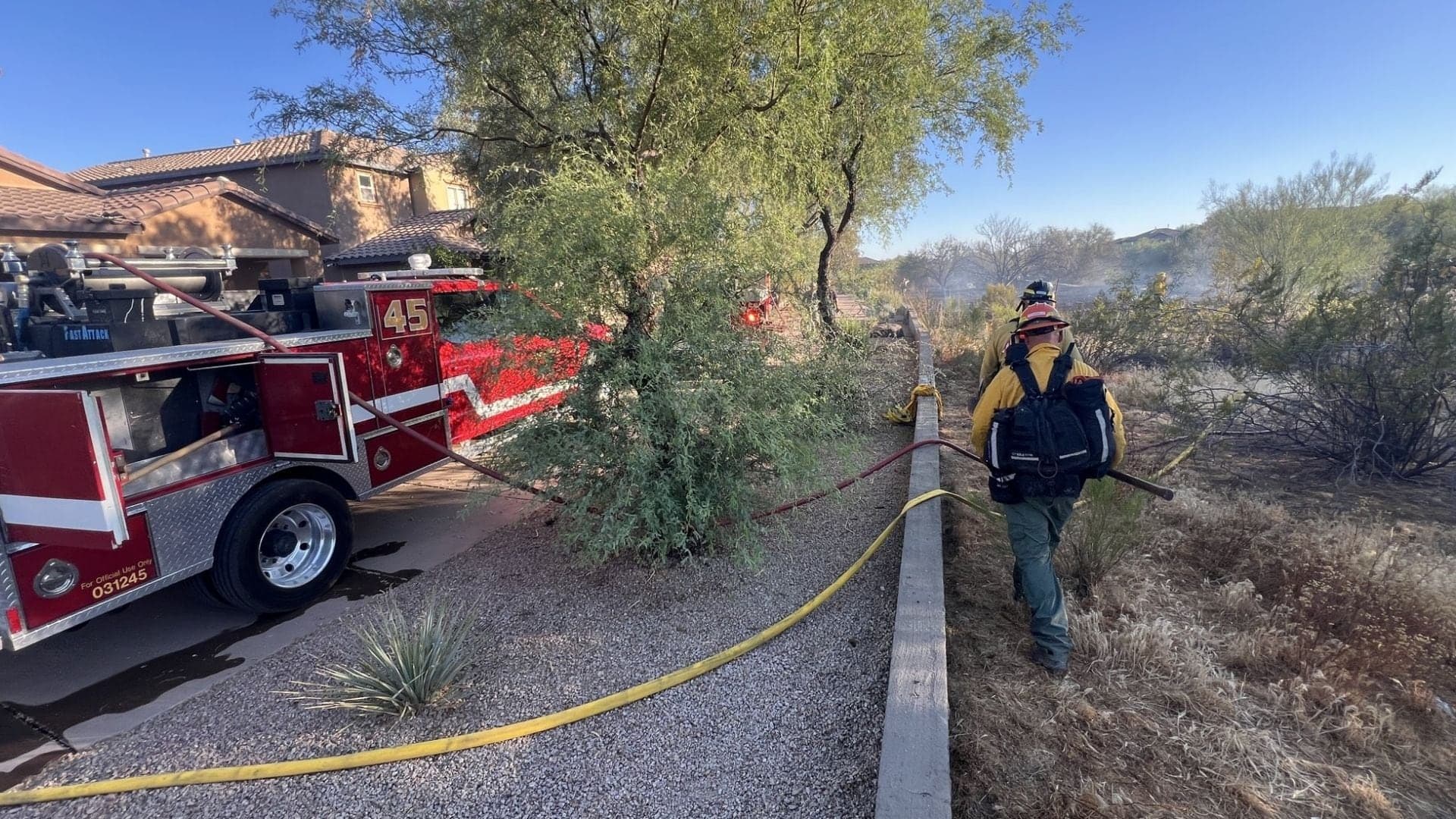Arizona firefighters and Engine 45 deploy hoses along a neighborhood edge while working a nearby brush fire as crews stage resources ahead of the Fourth of July weekend.