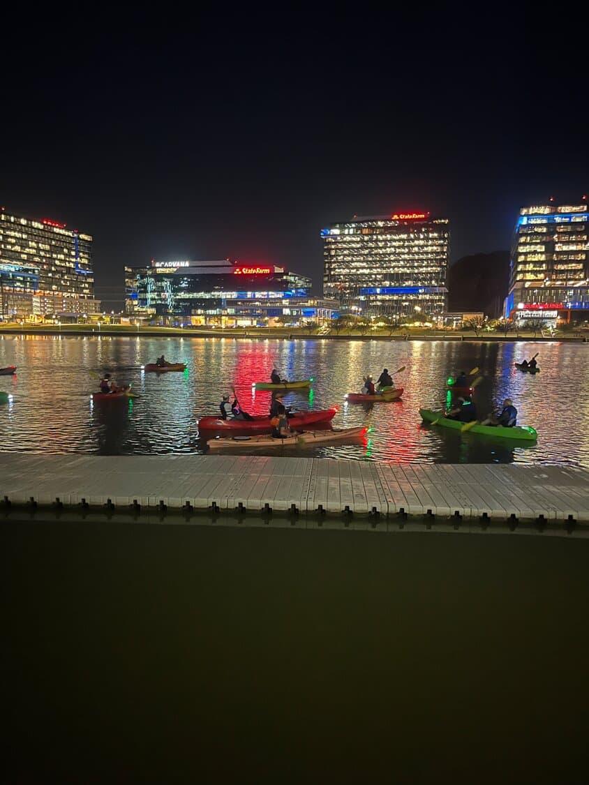 Kayakers on Tempe Town Lake at night with the illuminated downtown office buildings reflecting on the water — a popular recreational spot in Tempe.