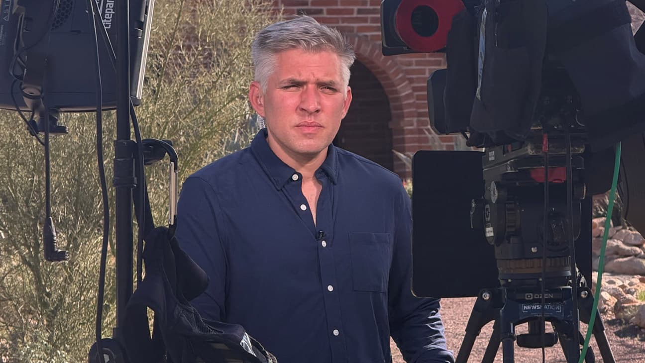 A field reporter stands between camera and lighting equipment during an on-location report outside a residence tied to the Nancy Guthrie kidnapping investigation.