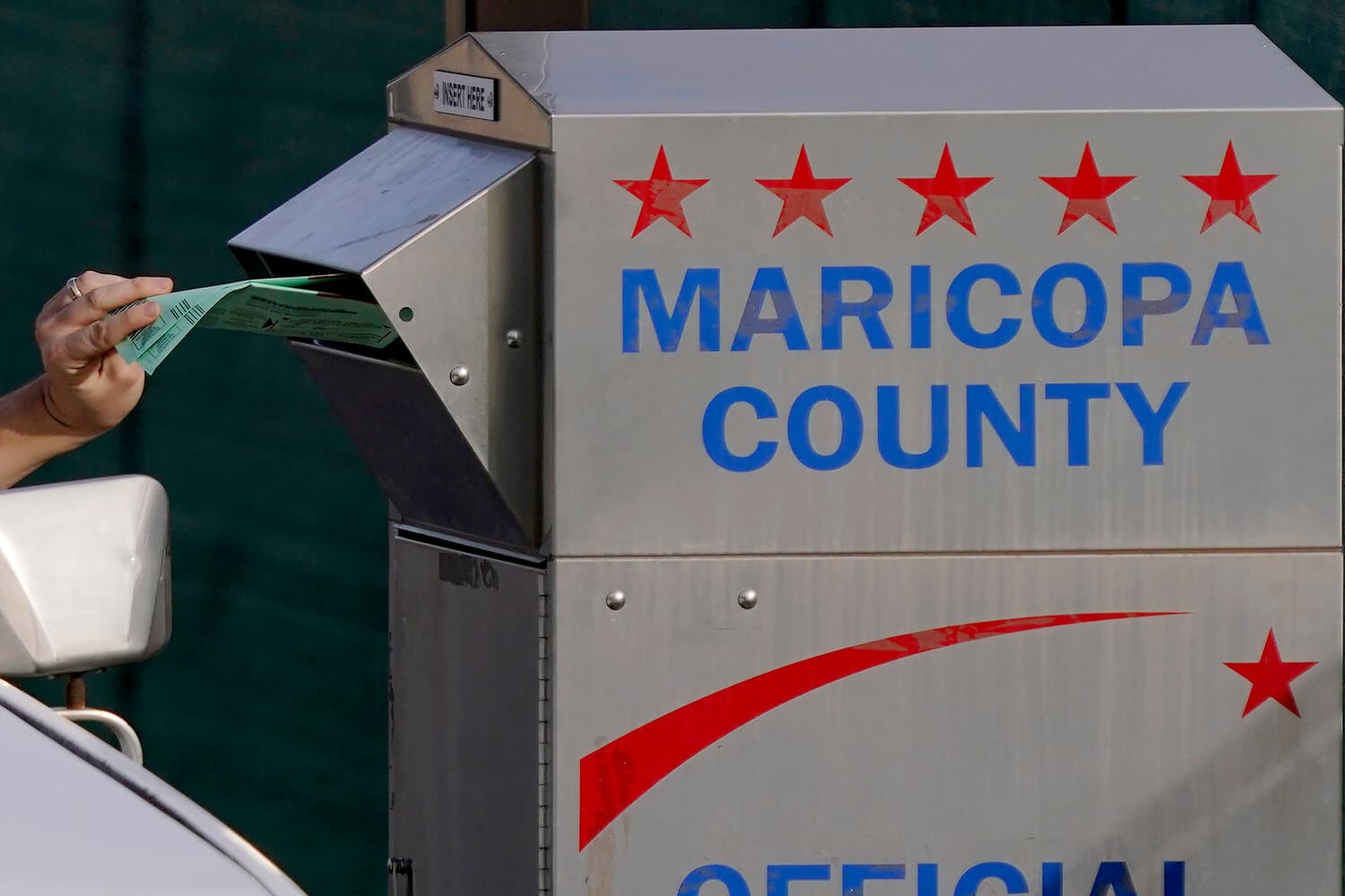 A voter deposits a mail ballot into a Maricopa County drop box during early reporting in the Arizona CD5 Democratic primary.
