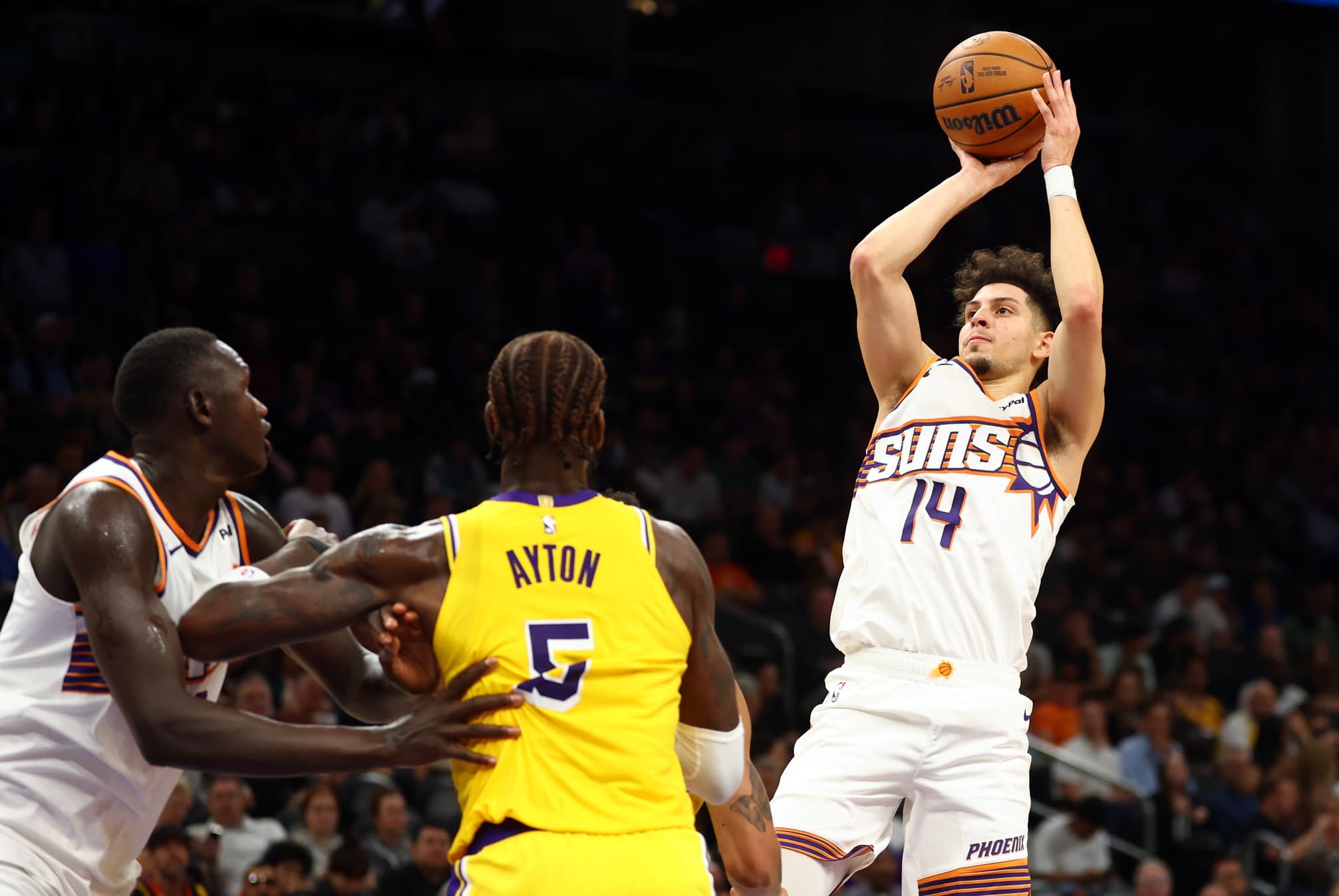 A Phoenix Suns player rises for a jumper over Los Angeles Lakers defenders during an NBA game — the Suns recently re-signed a guard to a two-way contract to bolster roster depth.