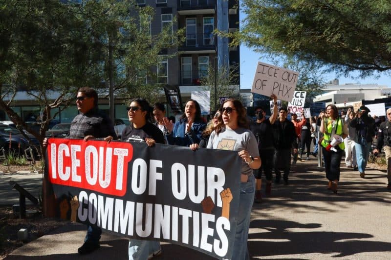 Protesters march down a sidewalk in Arizona carrying a banner reading “ICE OUT OF OUR COMMUNITIES,” illustrating local demonstrations referenced in this week’s events roundup.