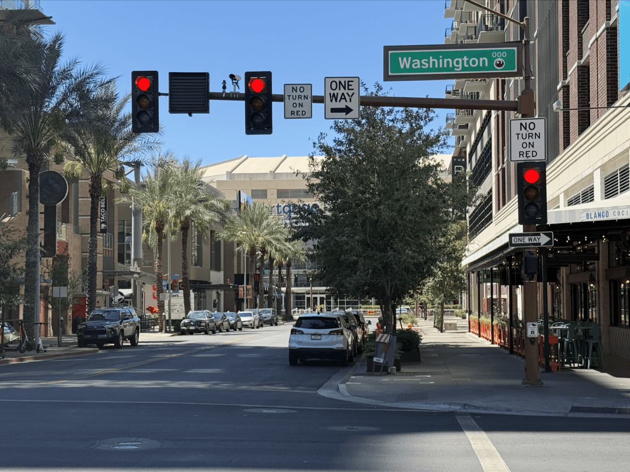 Washington Street sign above a downtown Phoenix intersection, with palm-lined sidewalks and storefronts — illustrating one of the president-named streets in the city.