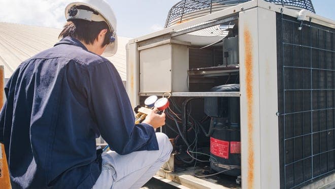 A technician checks pressure gauges on a rooftop AC unit during maintenance, highlighting the upkeep tied to rooftop cooling systems in Arizona's heat.