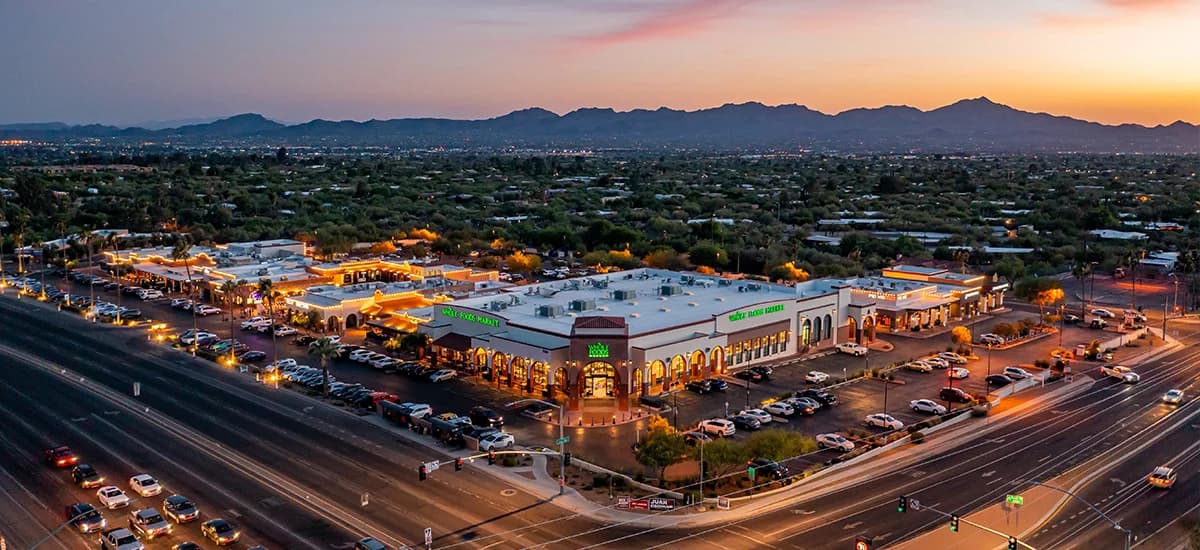 Oracle Crossing shopping center at dusk in Tucson, showing the Whole Foods Market anchor that fronts the grocery-anchored retail center sold for $54.35 million.