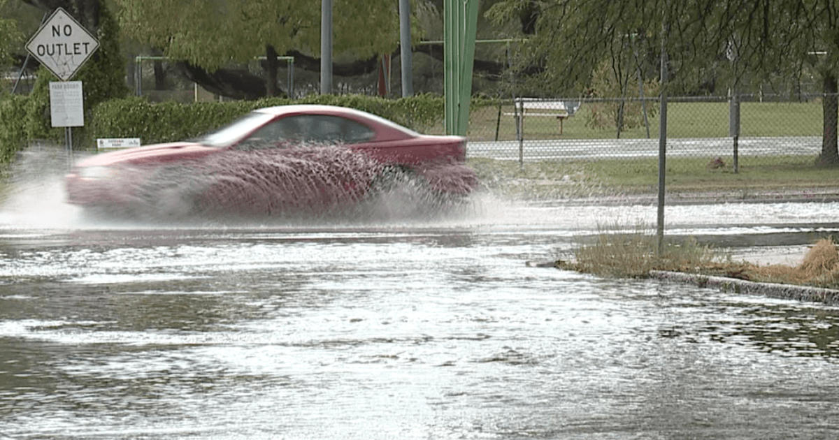 A car splashes through floodwater on a Tucson-area street during monsoon rains, illustrating the localized flooding risk described in the forecast.
