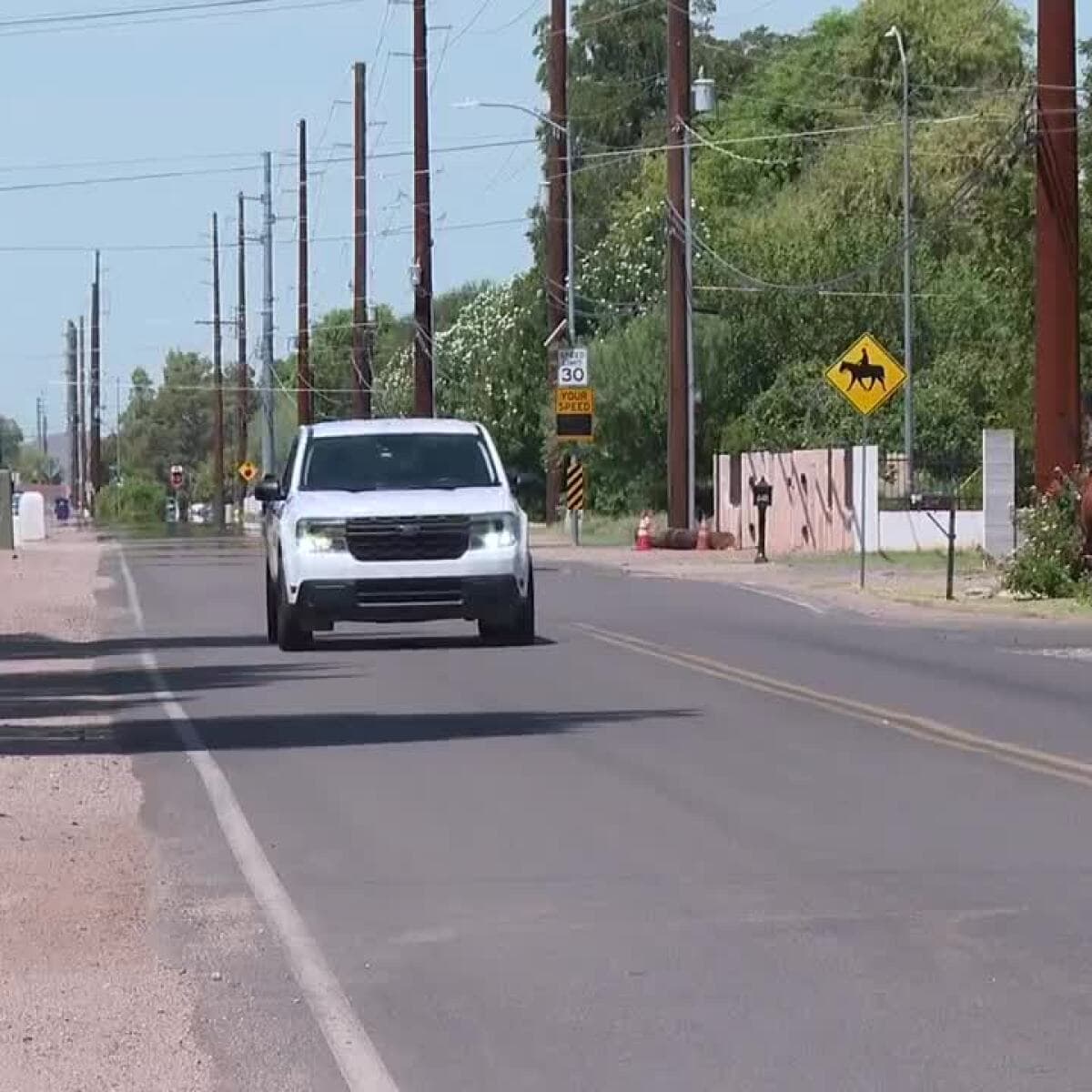 A vehicle nears a newly posted 30 mph sign in Mesa’s historic Lehi neighborhood while a rider travels on the road shoulder, illustrating residents’ safety concerns that prompted the speed-limit change.