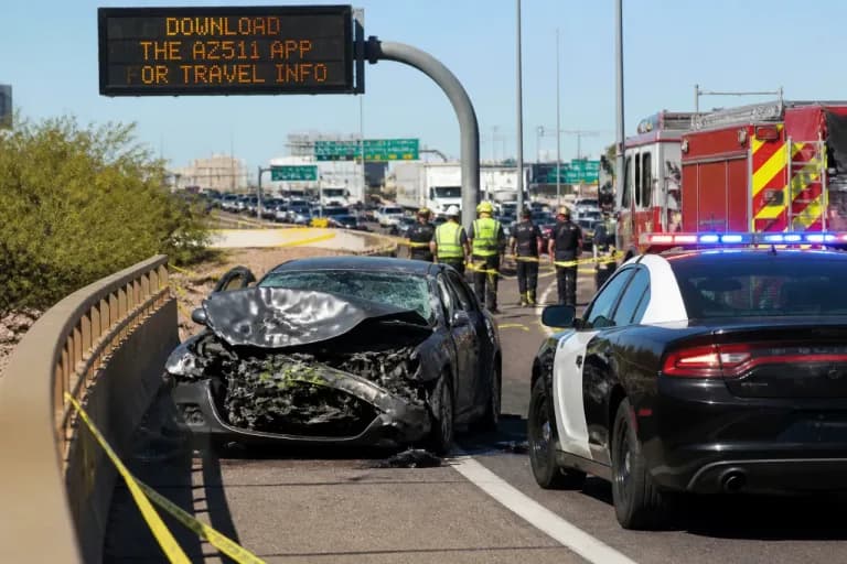 A heavily damaged sedan sits on the ramp with a Mesa police cruiser and fire truck nearby as first responders secure the scene following the fatal crash that closed the interchange.