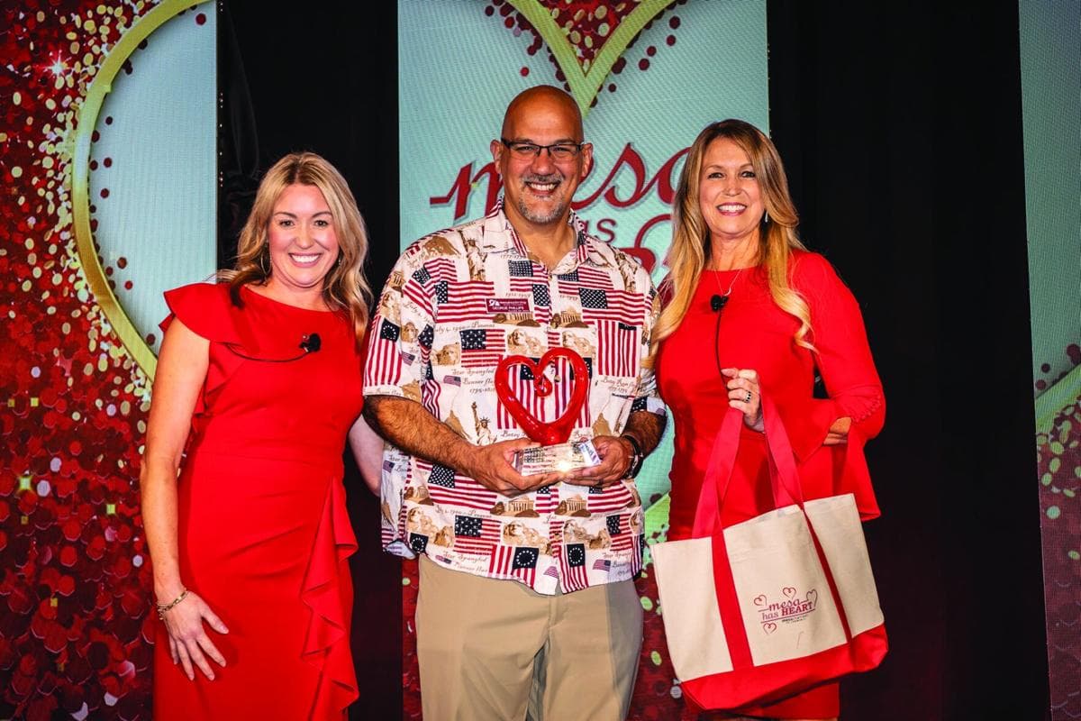 An award recipient holds a heart-shaped trophy flanked by two presenters onstage at the Mesa Chamber's 'Mesa Has Heart' awards gala.