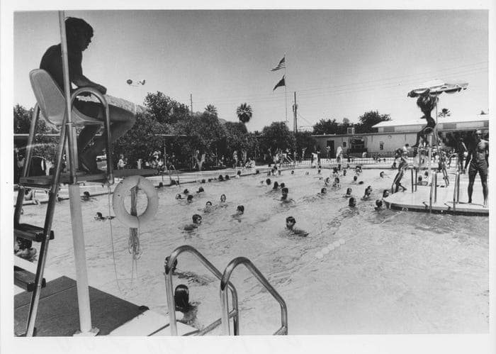 Mid-20th-century image of a busy public pool with a lifeguard chair and numerous swimmers, showing continued recreational use of Arizona's older pools.