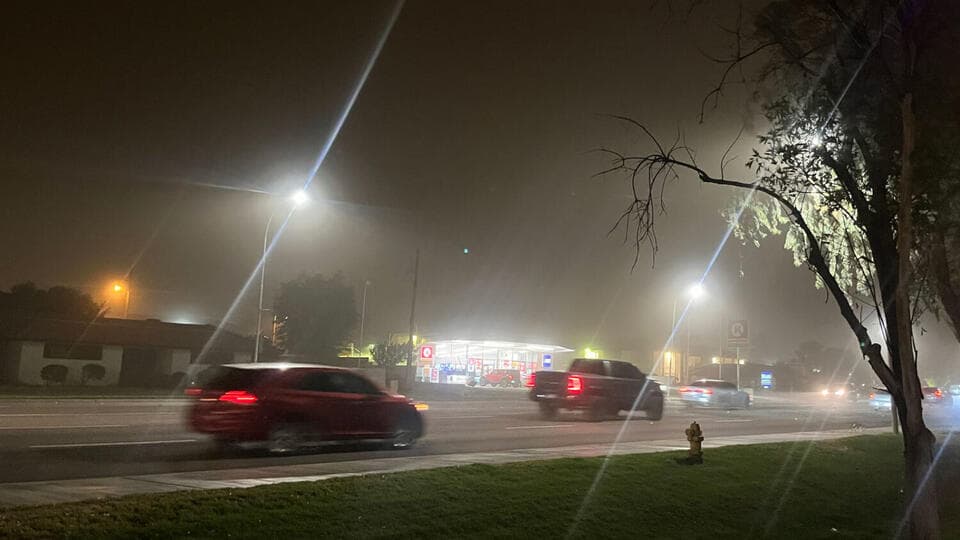 Drivers pass a gas station at night as dust and strong winds blow through Phoenix, visibly reducing roadway visibility during the dust storm.