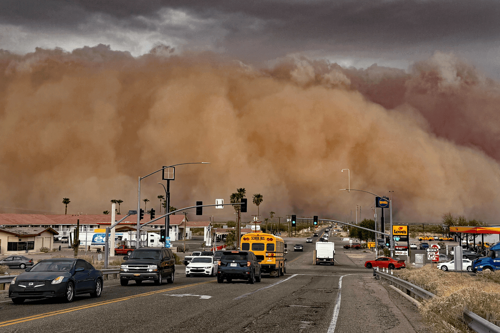 Motorists, including a school bus, approach an advancing dust storm on a Phoenix roadway — part of the same event that sent air quality readings far above normal.