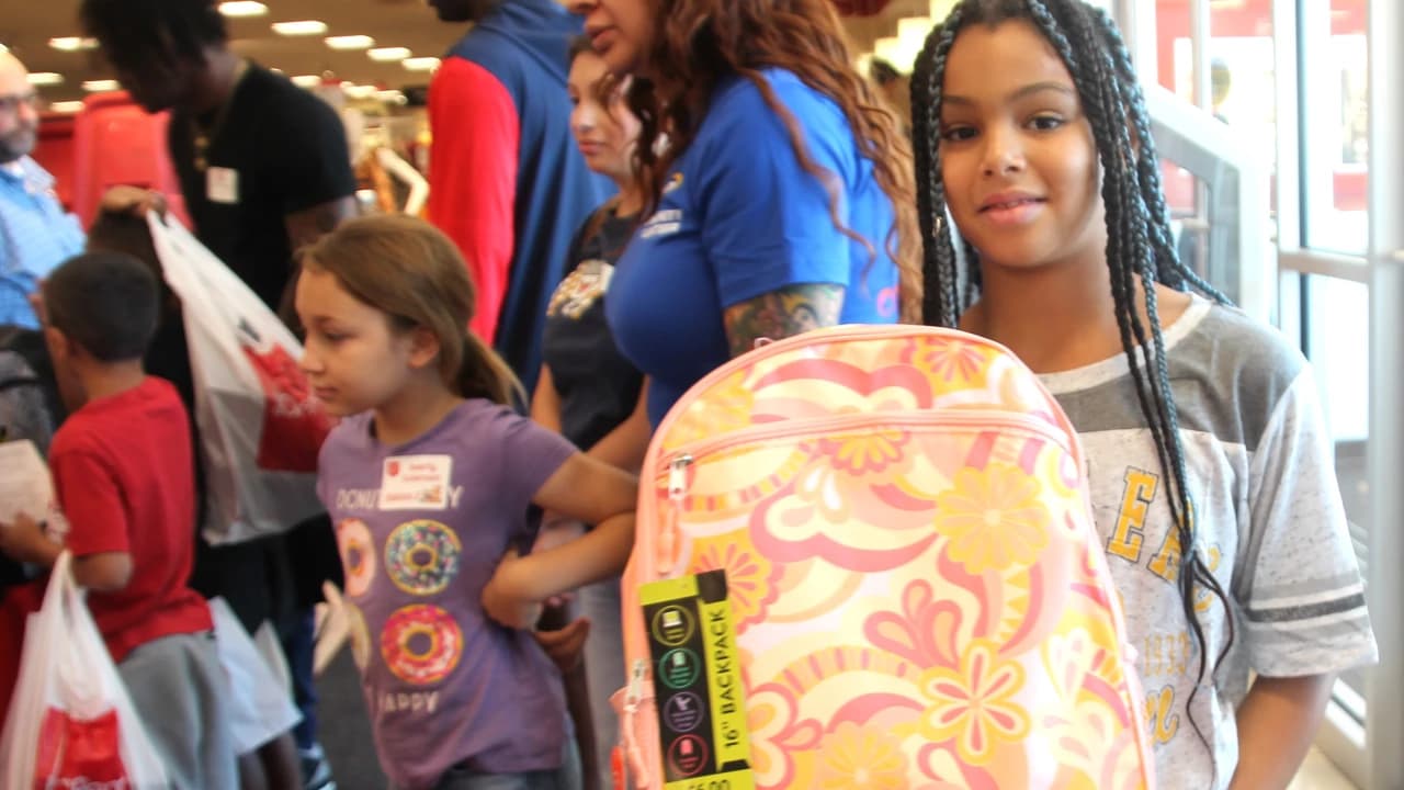 A student holds a donated backpack while volunteers and other children line up during the Salvation Army, Fry’s and KGUN 9 Back-to-School 'Backpack SOS' supply drive in Tucson.
