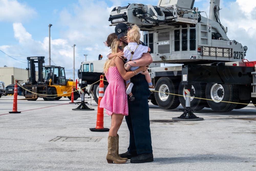 A crew member from USS Tucson embraces family on the pier during the submarine’s arrival at Naval Base Guam, capturing the personal side of the forward‑deployed homeport change.
