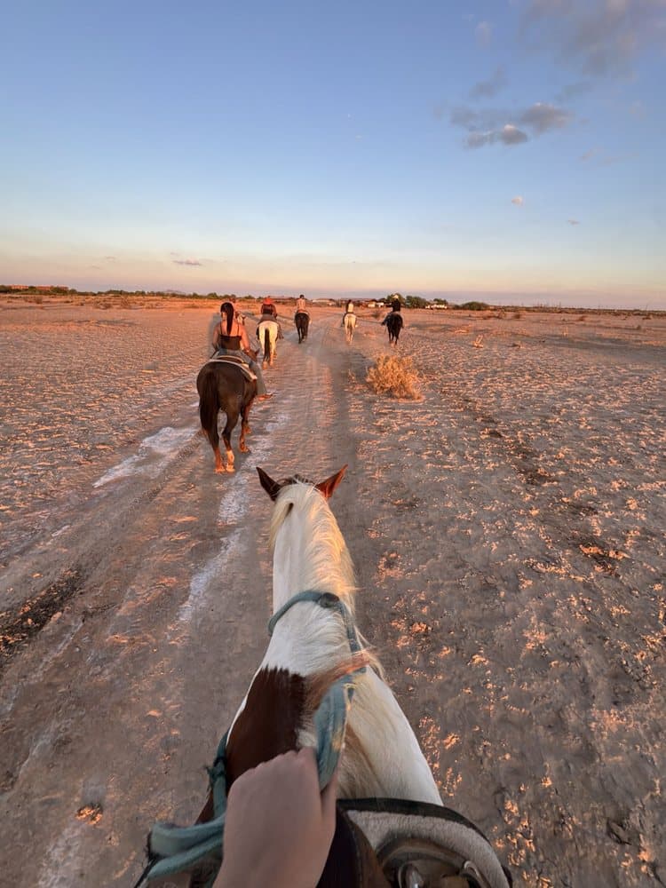A rider’s view of a guided group ride across arid terrain near Phoenix, showing participants on the Koli Equestrian Center experience that highlights Indigenous sites and stories.