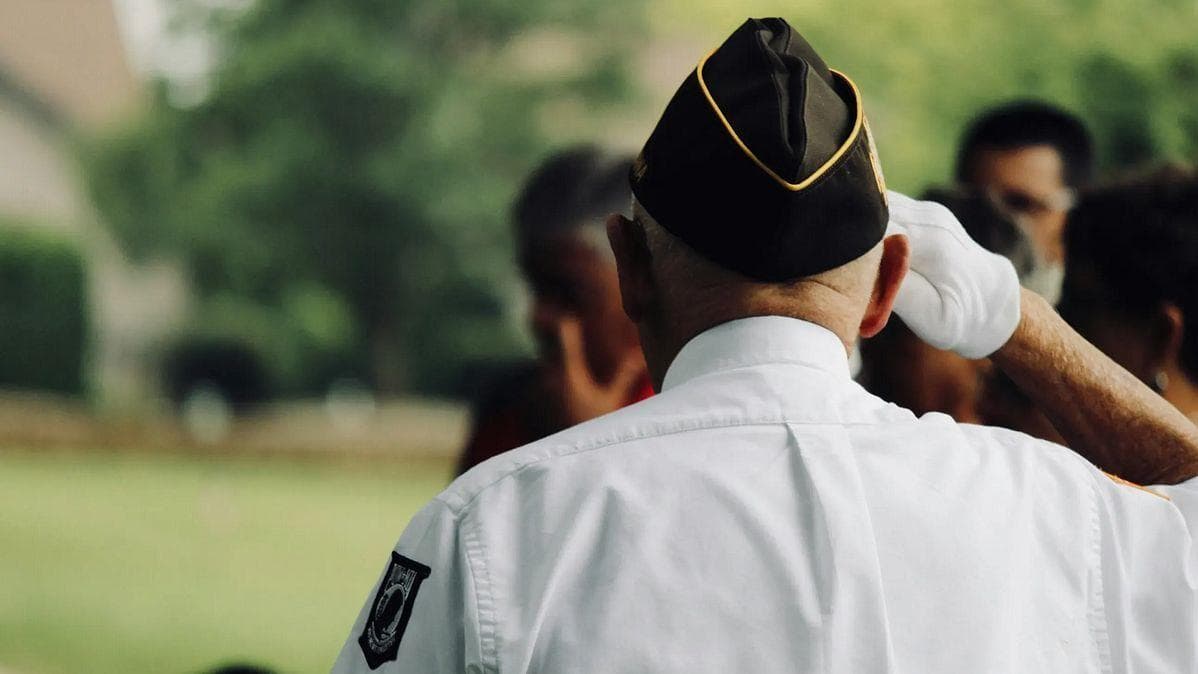 A military veteran in uniform salutes during a public ceremony, symbolizing the service members who could be affected by proposed increases to hazard pay.