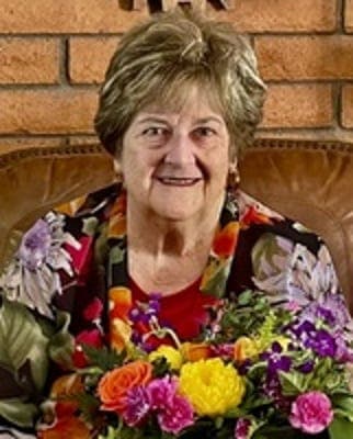 Indoor portrait of an older woman seated on a couch holding a bouquet; image accompanies the obituary listing on azcentral.com.