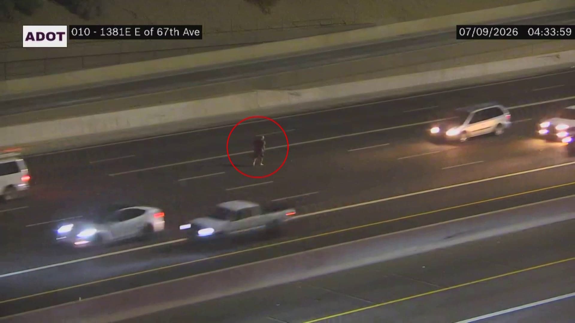 Aerial traffic camera image (ADOT) showing a man running in the westbound lanes of I‑10 near 67th Avenue in Phoenix shortly before he was struck, timestamped 07/09/2026 04:33:59.