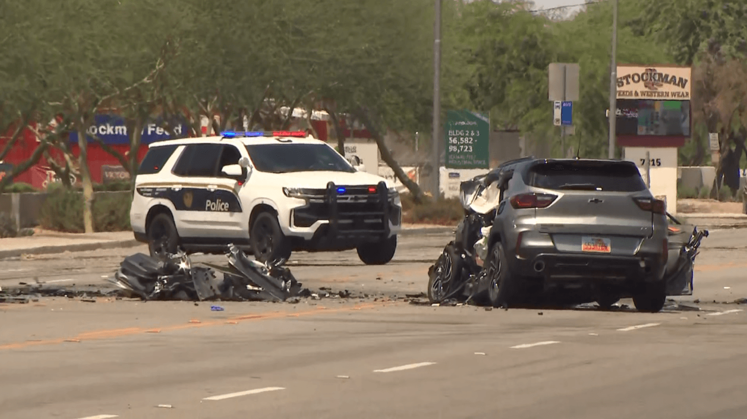 Police vehicle and a heavily damaged SUV at the crash scene in west Phoenix, with debris visible on the roadway as responders work.