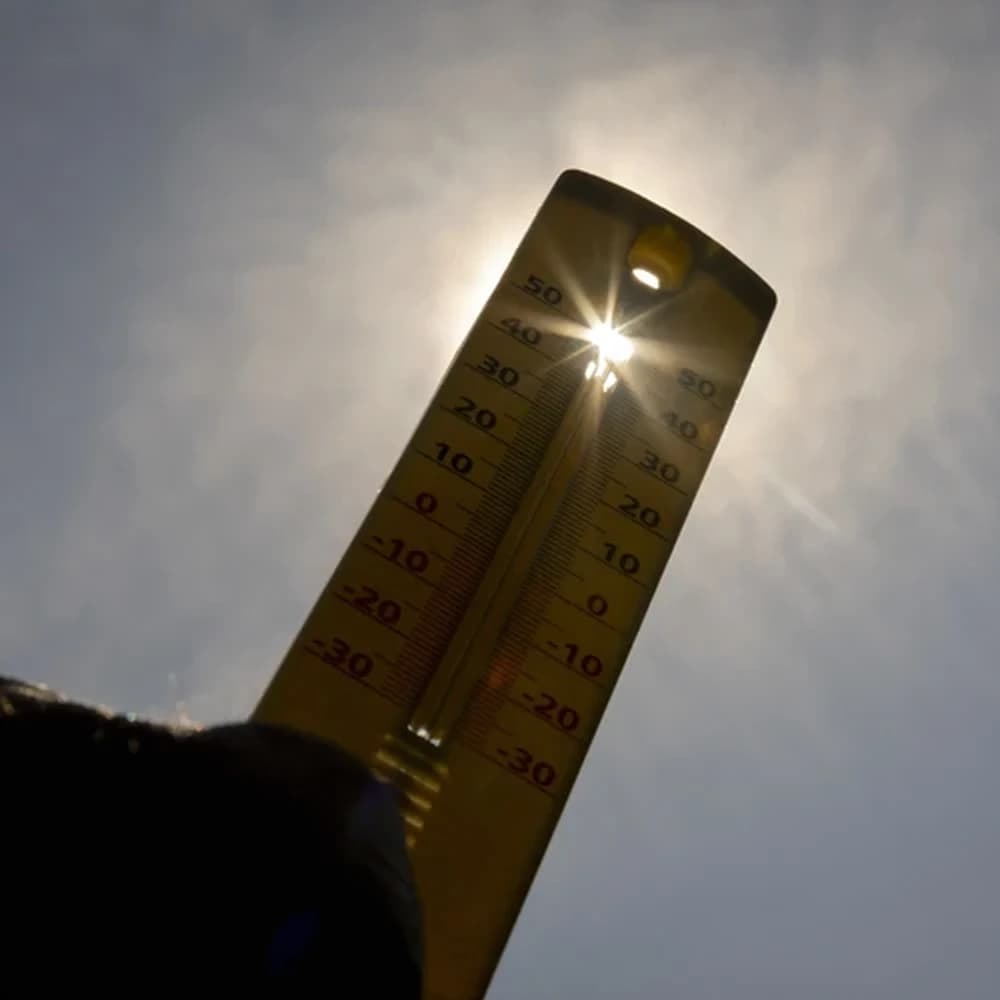 A handheld thermometer held up to the sun with a bright sun flare, visually representing the very hot temperatures expected across Arizona this week.