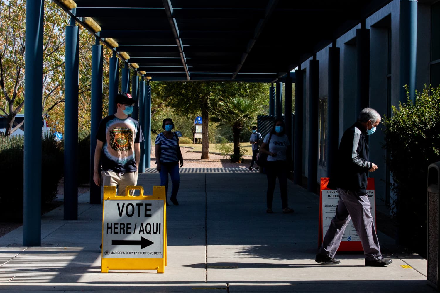 Voters walk past a 'VOTE HERE / AQUI' sign outside a Maricopa County polling location — the county whose 2020 voter files were later copied in the reported hack.
