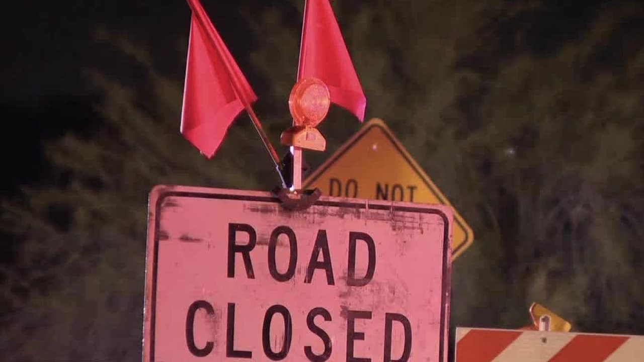 A 'Road Closed' sign and warning flags block a flooded roadway during monsoon storms in the Phoenix Valley, illustrating the hazards that can lead to penalties under Arizona's 'Stupid Motorist Law.'