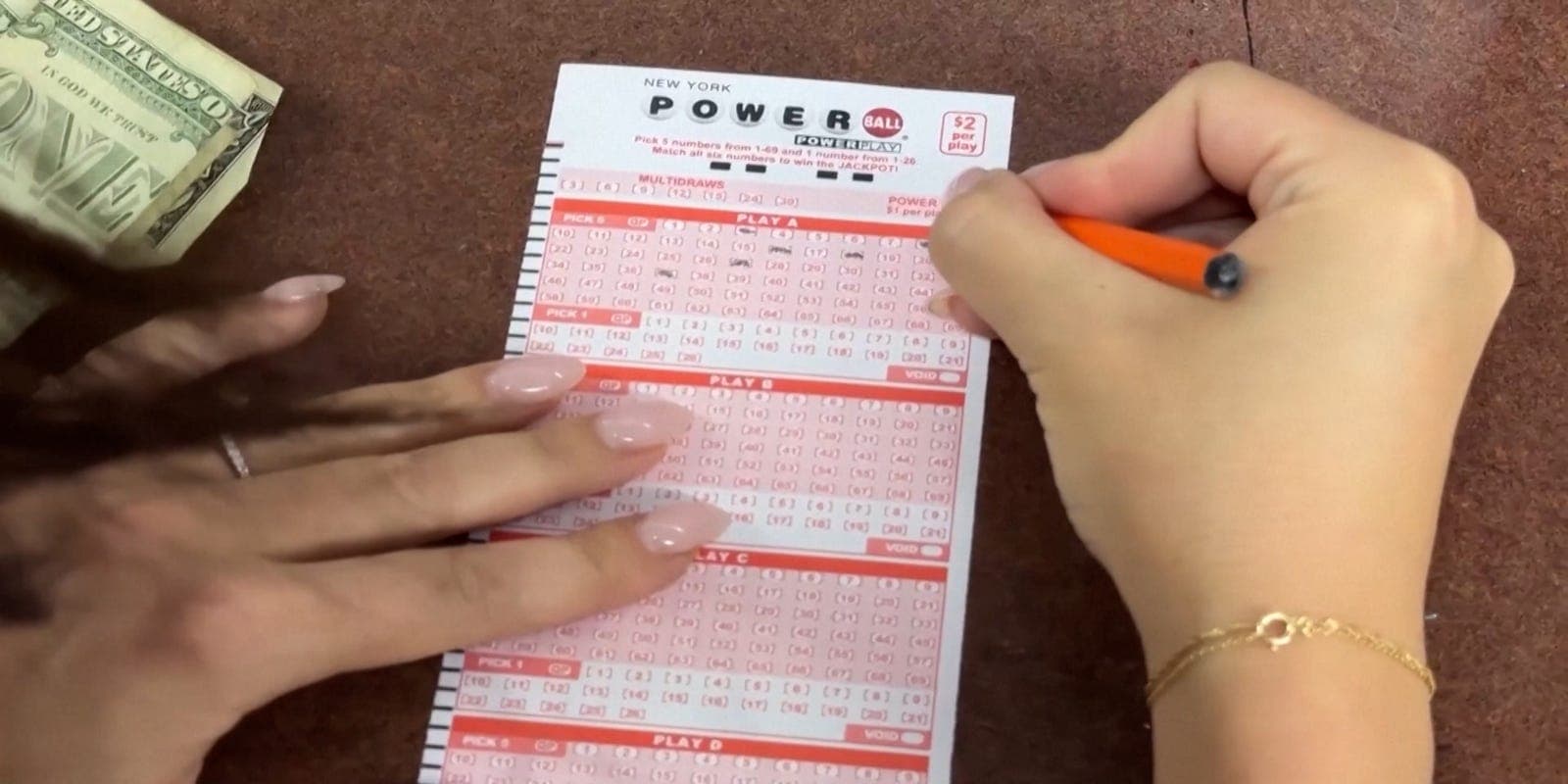 A player fills out a Powerball play slip with cash at hand as Arizona Lottery customers check tickets ahead of the July 4, 2026 drawing.