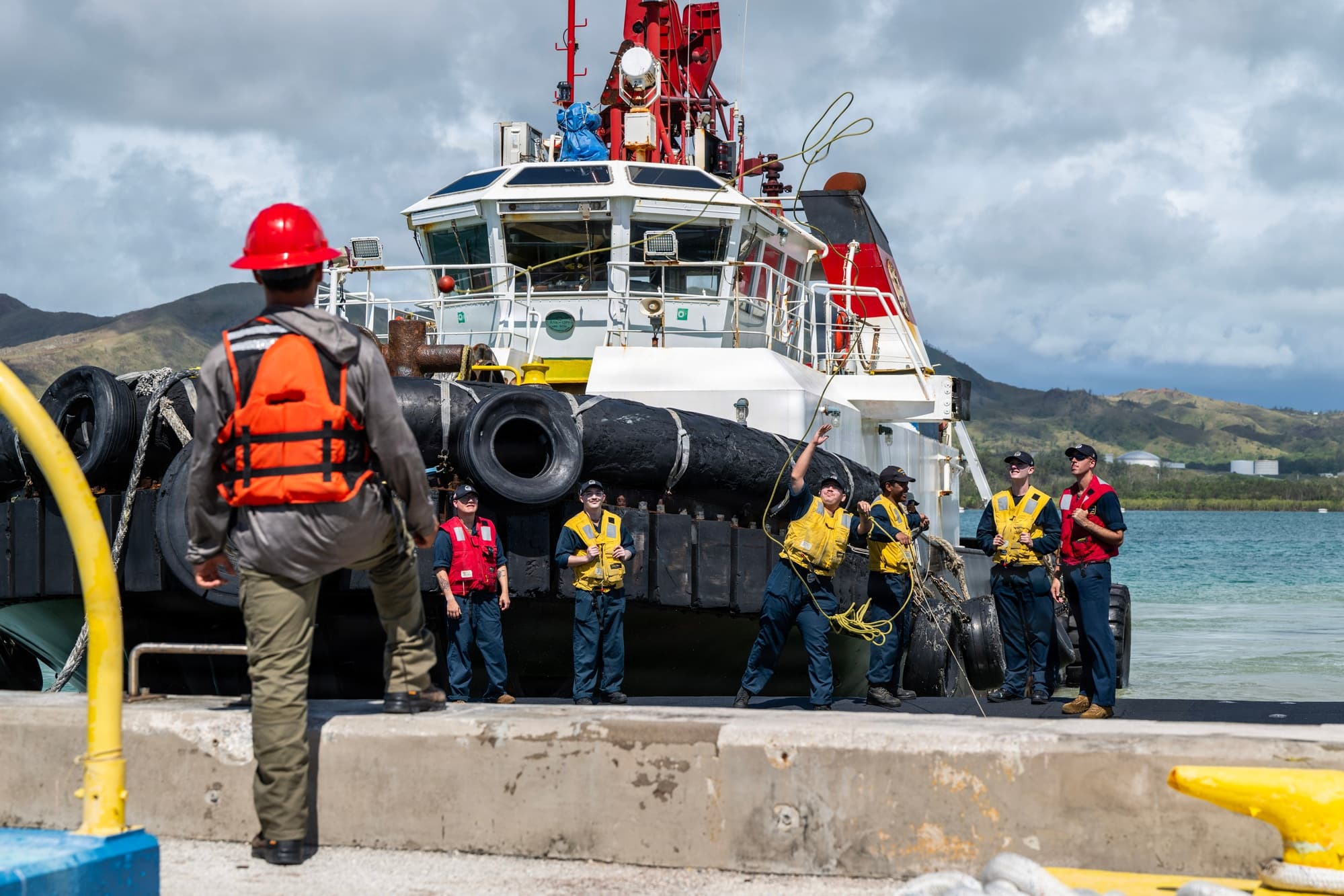 Sailors from the Los Angeles‑class fast‑attack submarine USS Tucson stand topside and alongside a tug as the submarine arrives and moors at Naval Base Guam during the July 10, 2026 homeport shift.