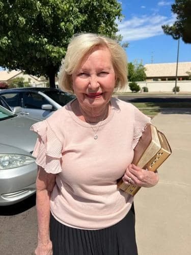 Obituary photo used with the article: an elderly woman standing in a parking lot in Gilbert, Arizona, holding a book.
